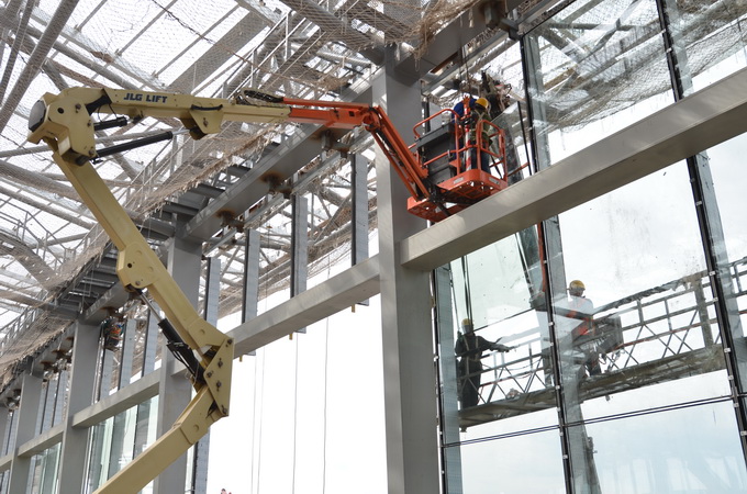 北京新机场西南指廊二层,四名工人正在十几米的高空吊装一块玻璃幕墙